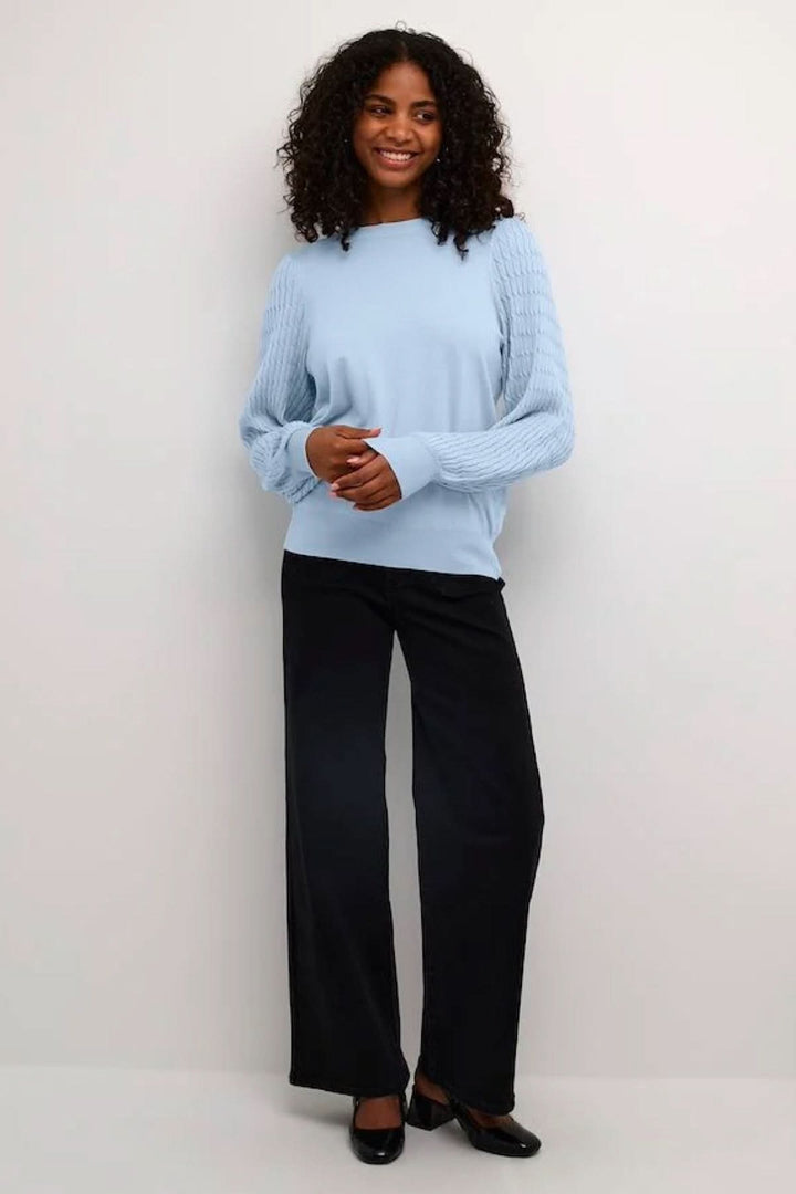 Chandail bleu avec manches côtelées et coupe décontractée, porté avec un pantalon noir élégant.
