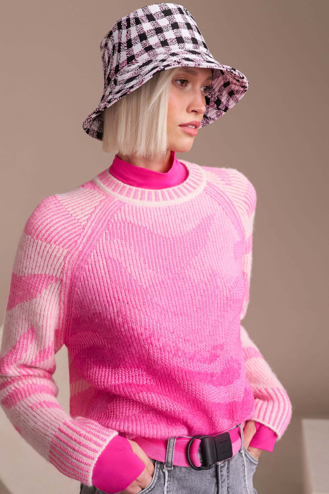 Chandail motif dégradé rose avec manches longues et encolure ronde, porté par une personne avec un chapeau à carreaux noir et blanc.