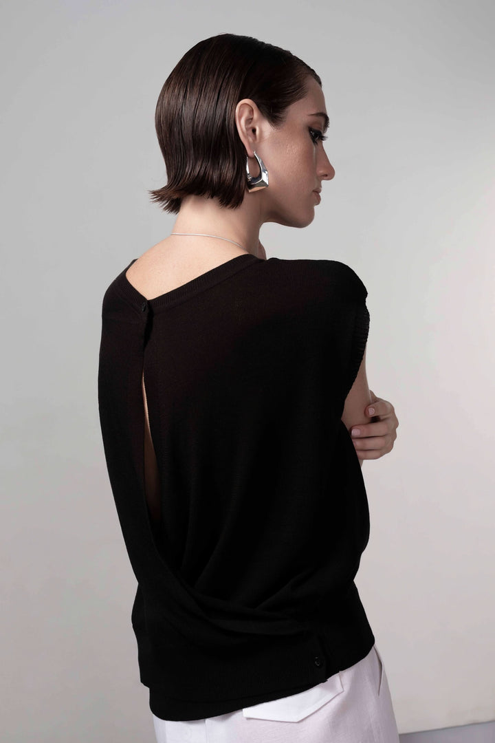 Femme portant un chandail ouverture au dos, sans manches, de couleur noire, avec un look contemporain et élégant.