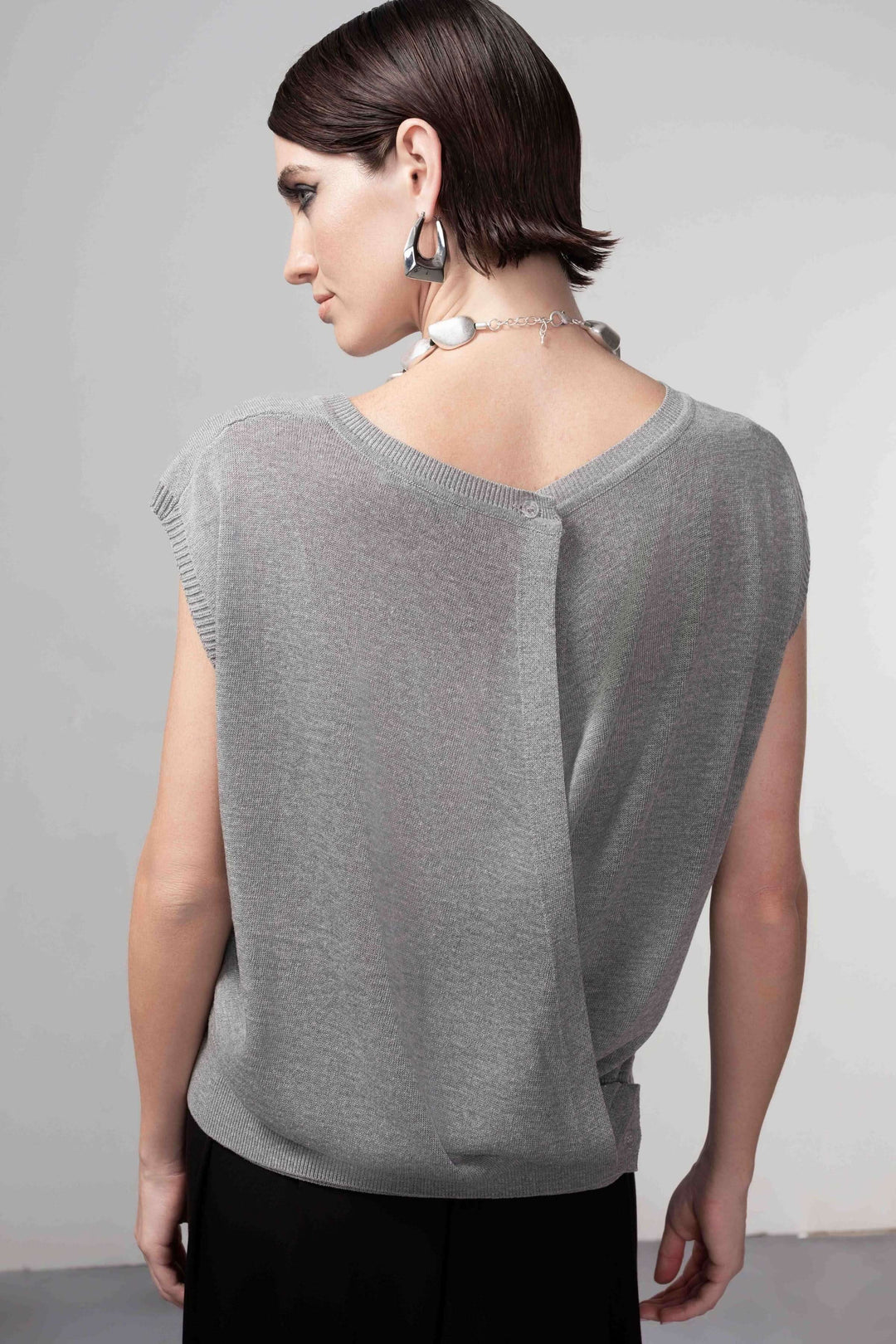 Femme portant un chandail ouverture au dos, maille fine, coupe droite, style contemporain et épuré, couleur grise.