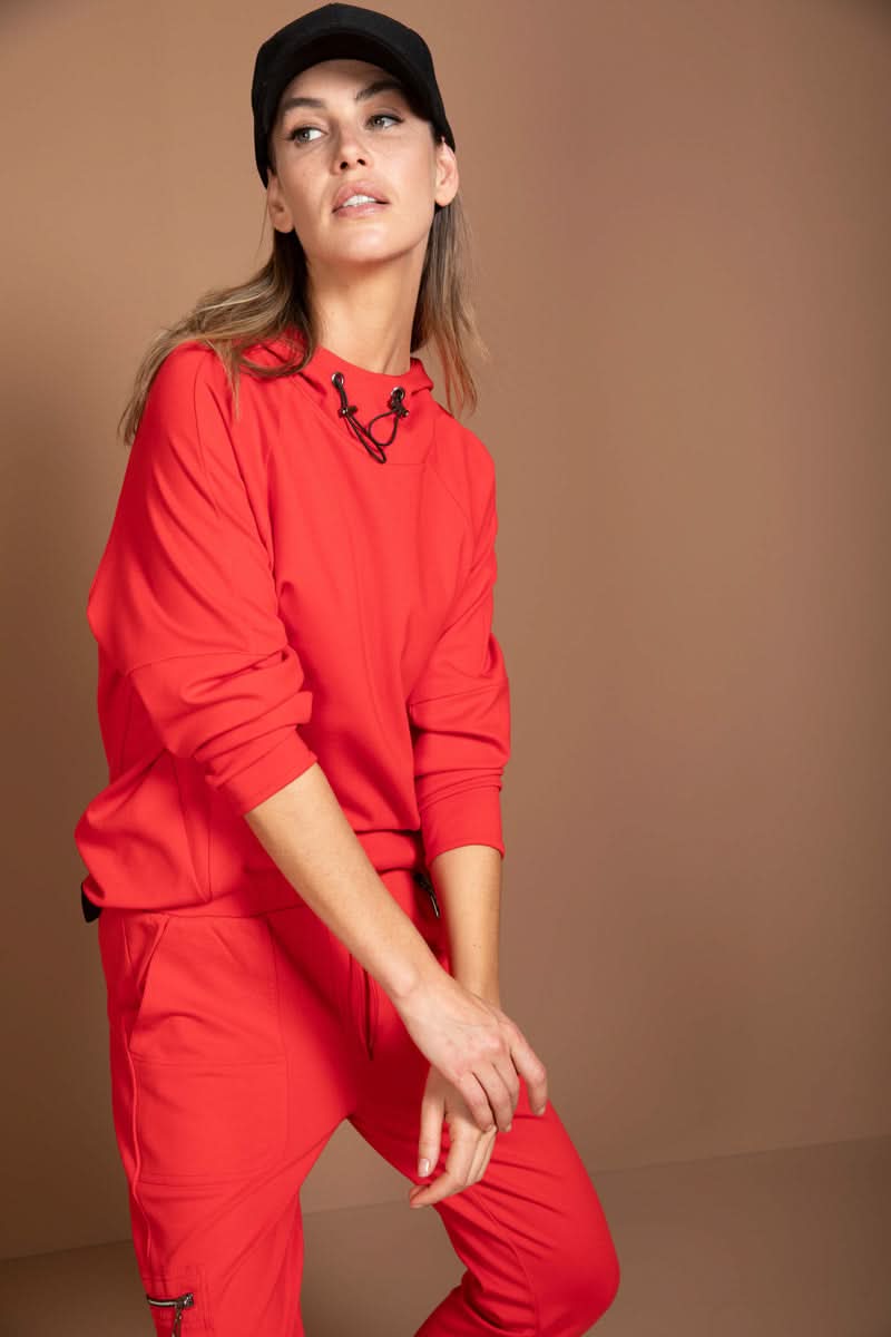 Femme portant un chandail structuré rouge au style athleisure avec col montant et cordon ajustable, idéal pour allure moderne et sportive.