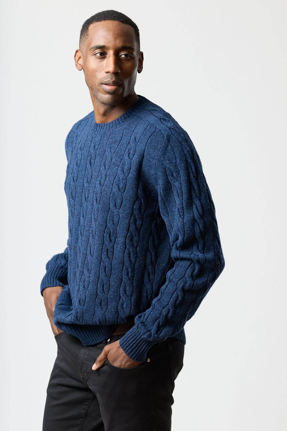 Homme portant un chandail torsadé col rond bleu avec texture câblée, style chic et décontracté.
