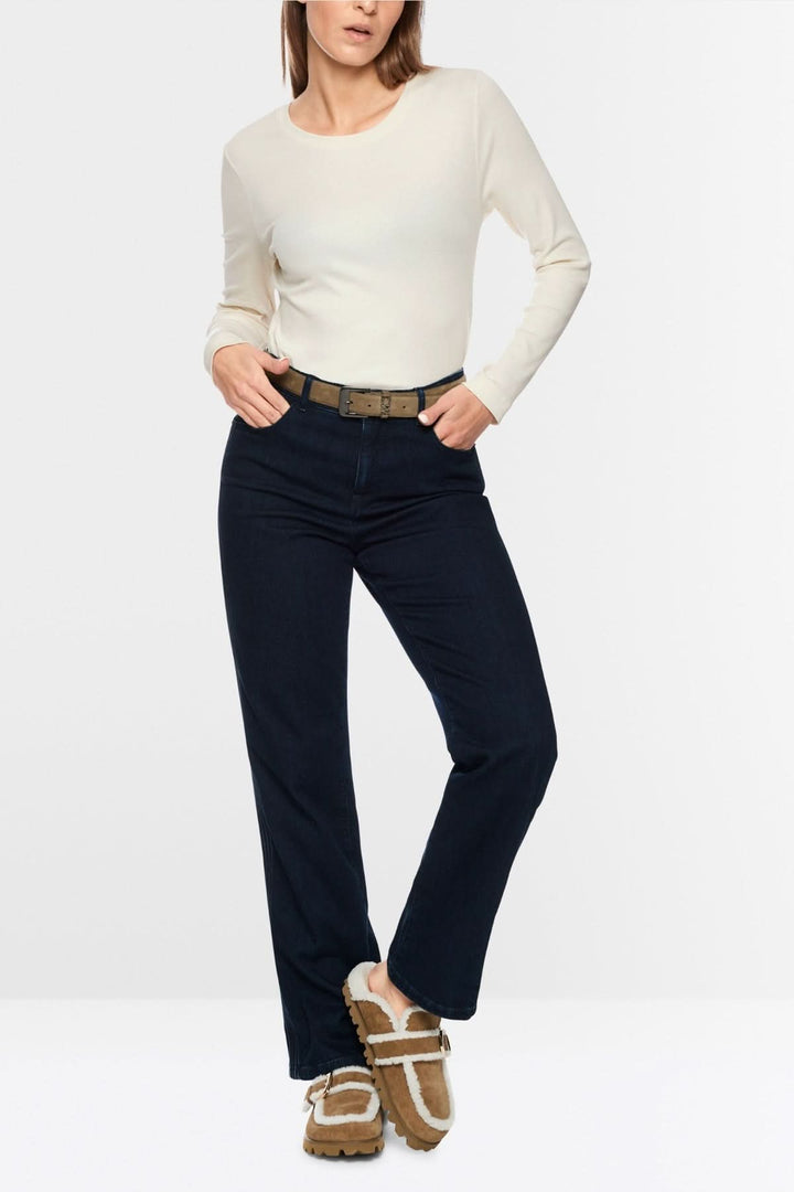 Femme portant un chandail unie à manches longues, taille ajustée, avec un jean foncé et des chaussures marron, style minimaliste et chic.