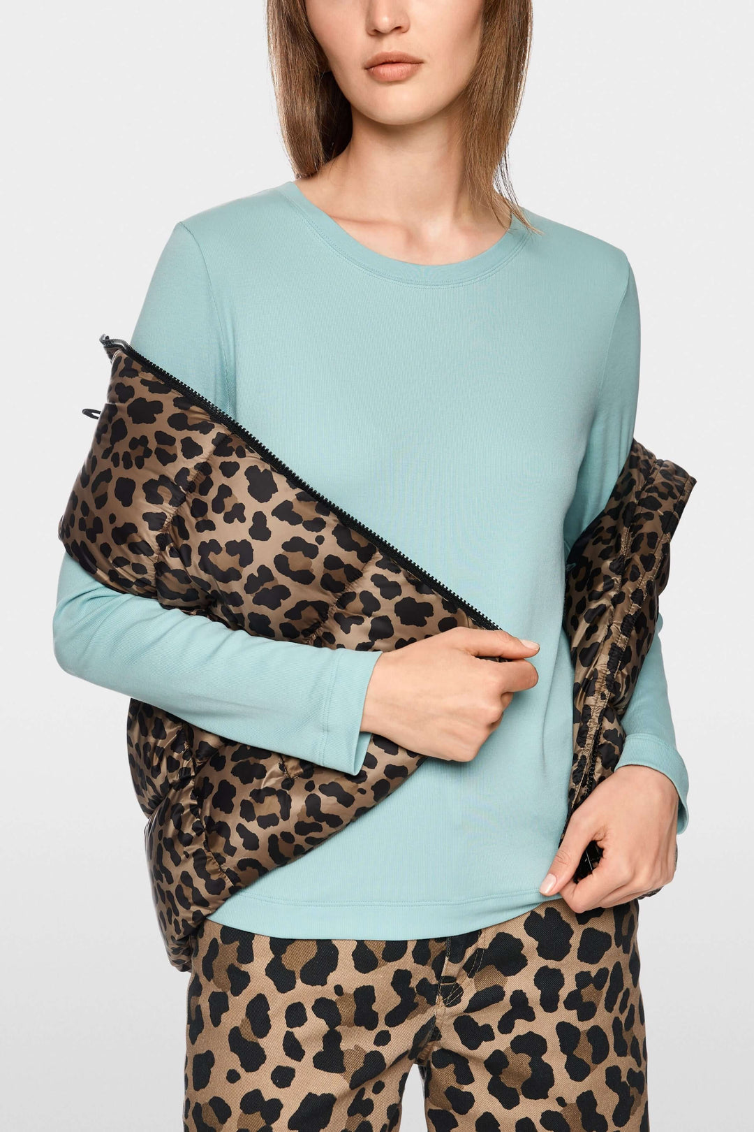 Femme portant un chandail unie à manches longues bleu avec une veste à imprimé léopard, look minimaliste et chic.