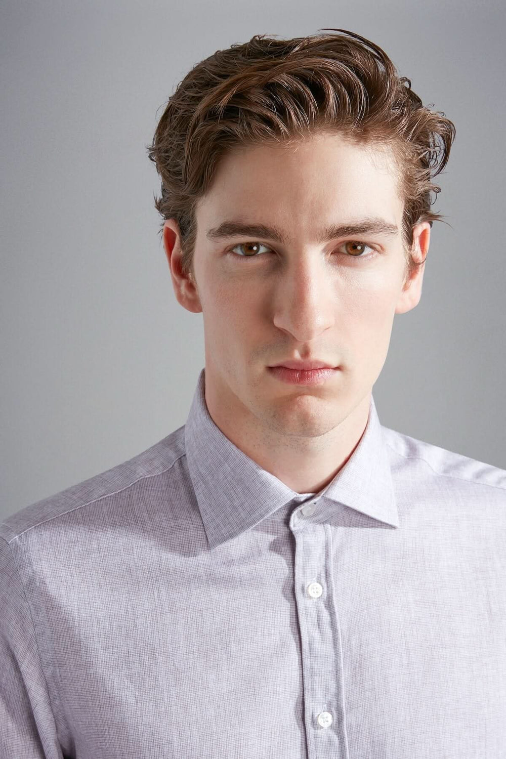 Homme portant une chemise habillée beige-gris à col classique et manches longues, regard sérieux.