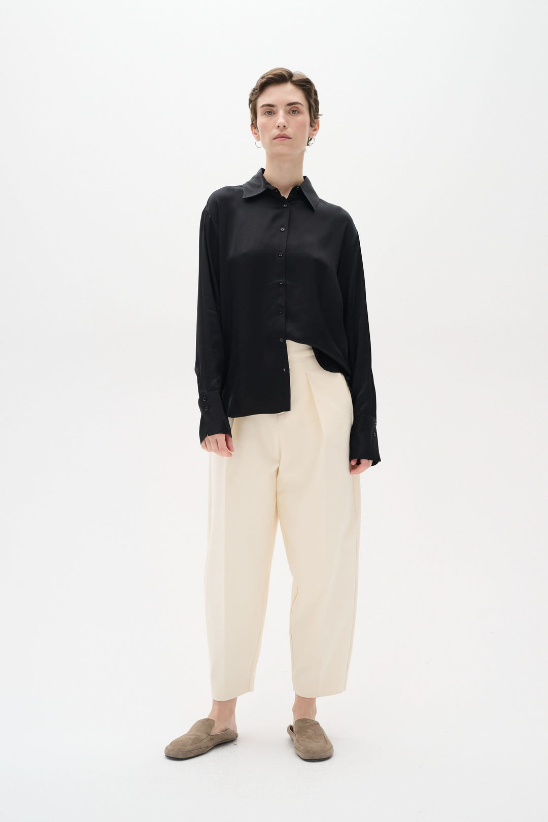 Chemise satinée noire portée avec un pantalon beigne, style chic et décontracté, sur fond blanc.