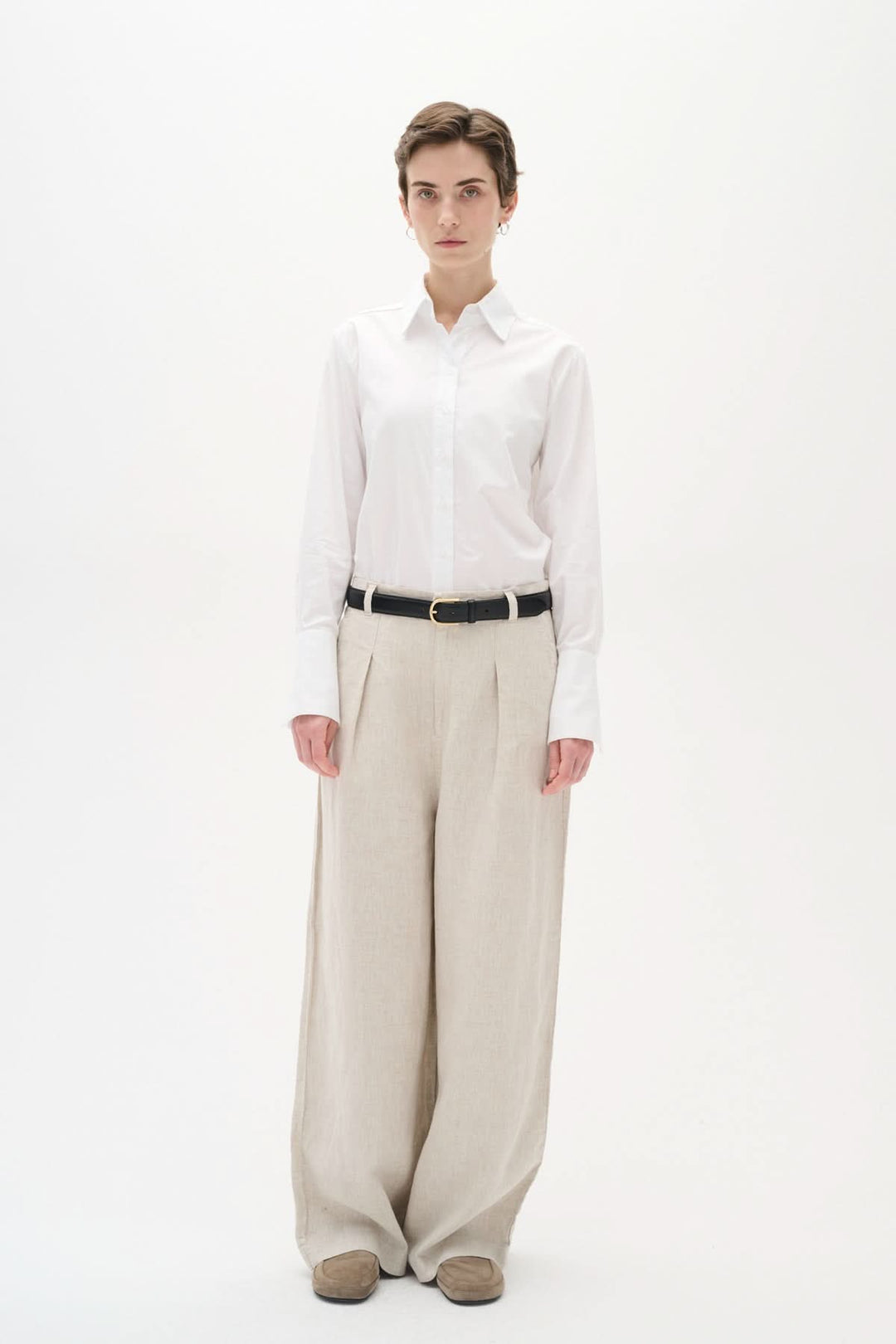 Modèle portant une chemise blanche classique, pantalon large beige et ceinture noire, pour un look élégant.