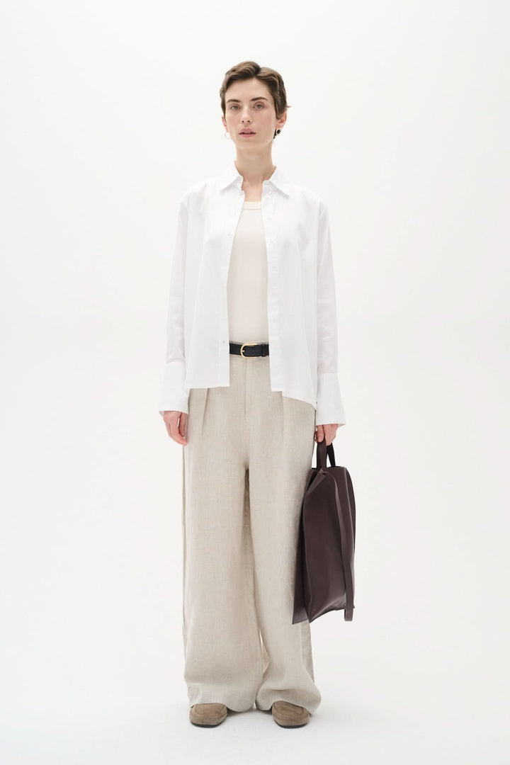Mannequin portant une chemise blanche classique, pantalon beige et sac en cuir, pour un look élégant et moderne.