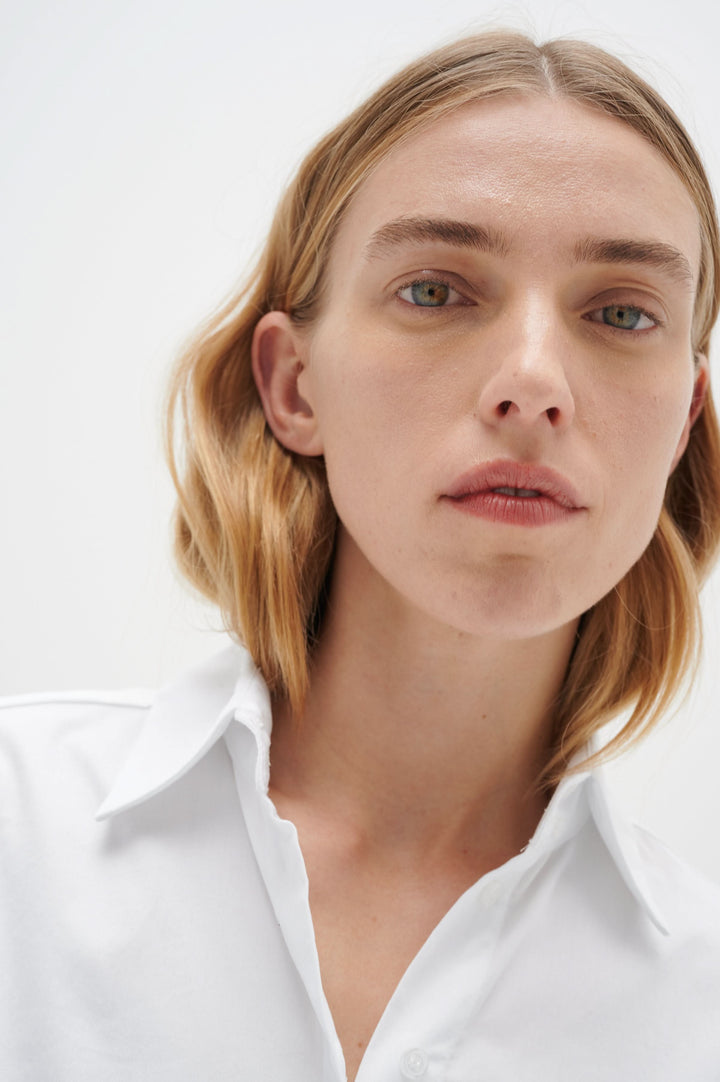 Femme portant une chemise blanche à manches longues, mettant en valeur le col traditionnel et le style élégant.