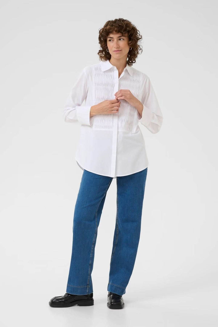 Femme portant une chemise classique avec plis nervurés, associée à un jean et des chaussures noires, offrant un style décontracté chic.