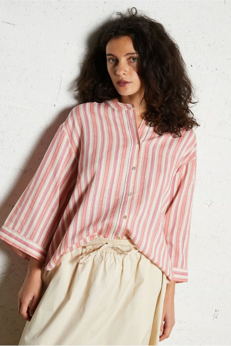 Femme portant une chemise design épuré à rayures roses et blanches avec coupe ample et manches longues.