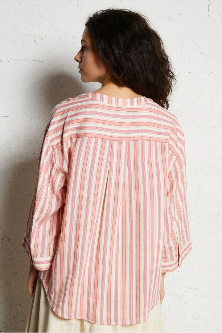 Femme portant une chemise à rayures roses et blanches, vue de dos, coupe décontractée et élégante.