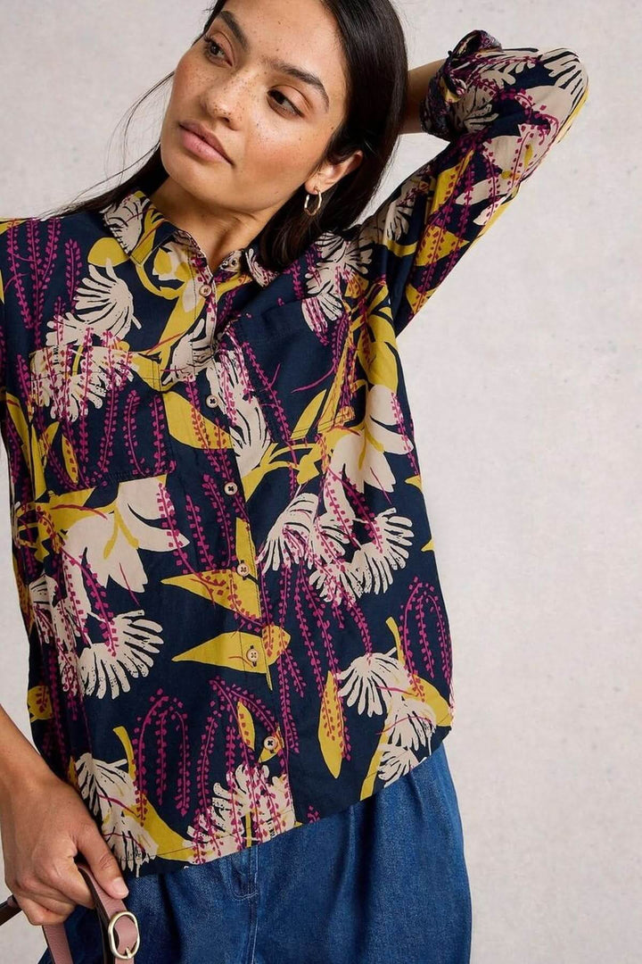 Femme portant une chemise imprimée colorée avec un col classique et manches longues retroussées, sur fond neutre.