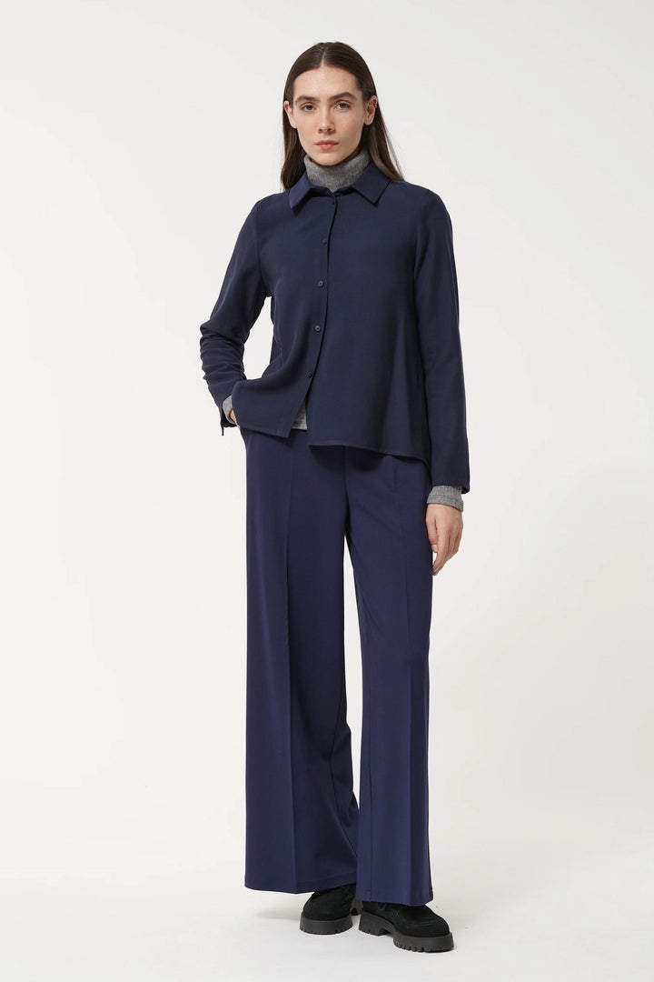 Femme portant une chemise fluide bleu avec pantalon large, style chic et minimaliste, col classique, fermeture boutonnée.
