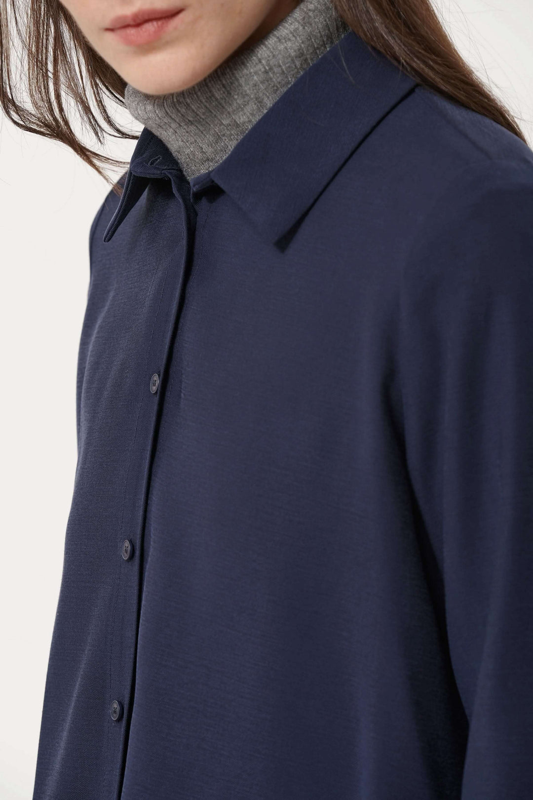 Chemise fluide bleue avec col classique et fermeture boutonnée, portée sur un col roulé gris pour un look élégant et polyvalent.