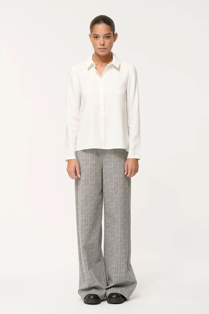 Chemise fluide élégante et confortable avec coupe ample, col classique et fermeture boutonnée, portée avec un pantalon large.