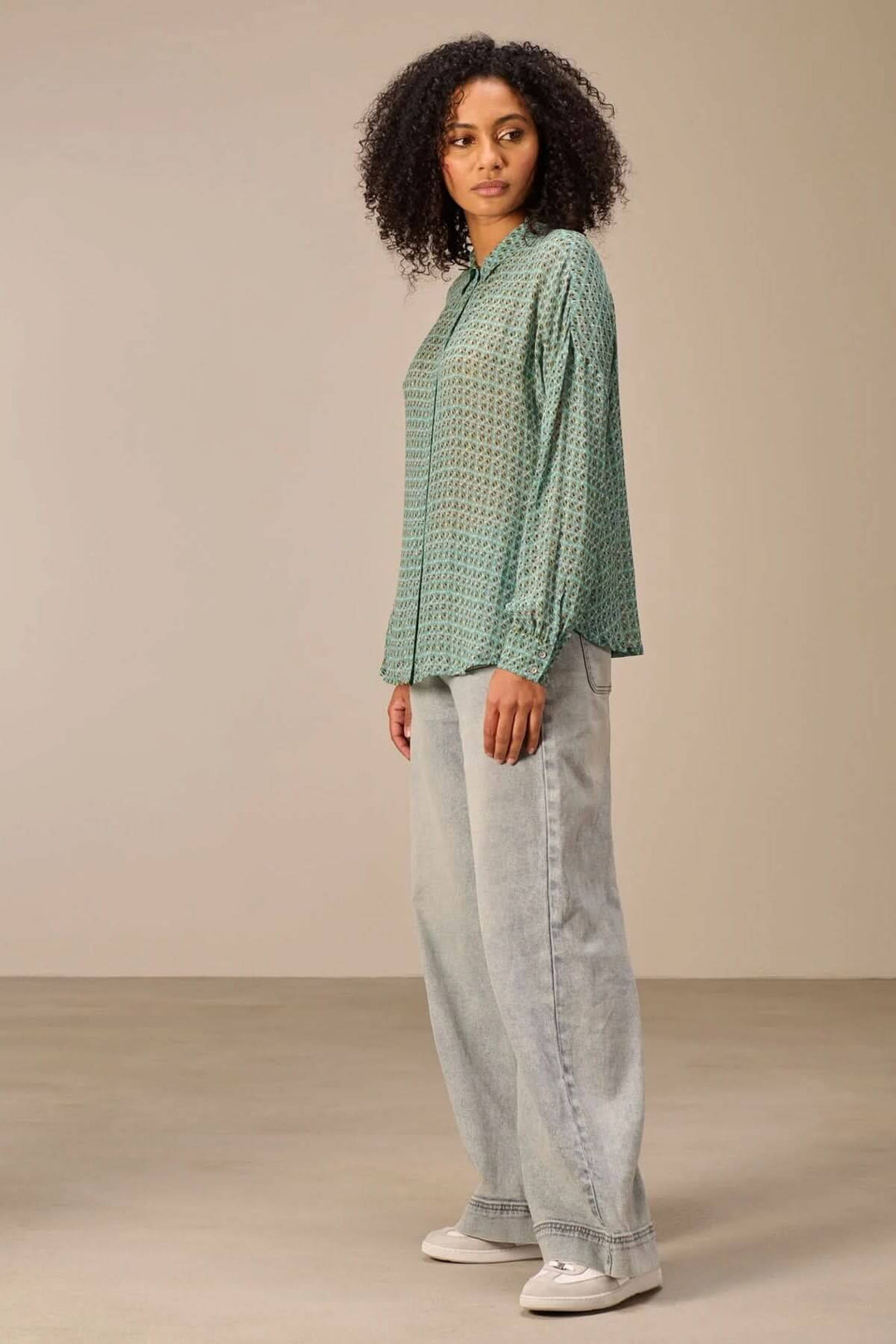 Femme portant une chemise fluide imprimé avec motif géométrique, coupe décontractée. Associe confort et élégance moderne.