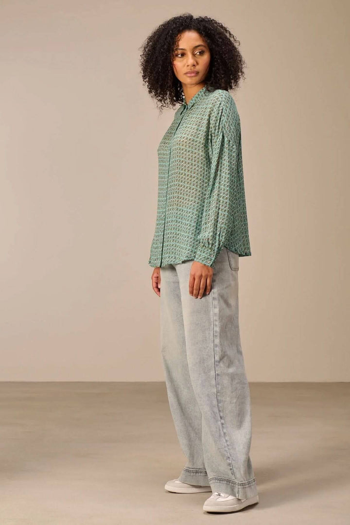 Femme portant une chemise fluide imprimé avec motif géométrique, coupe décontractée. Associe confort et élégance moderne.