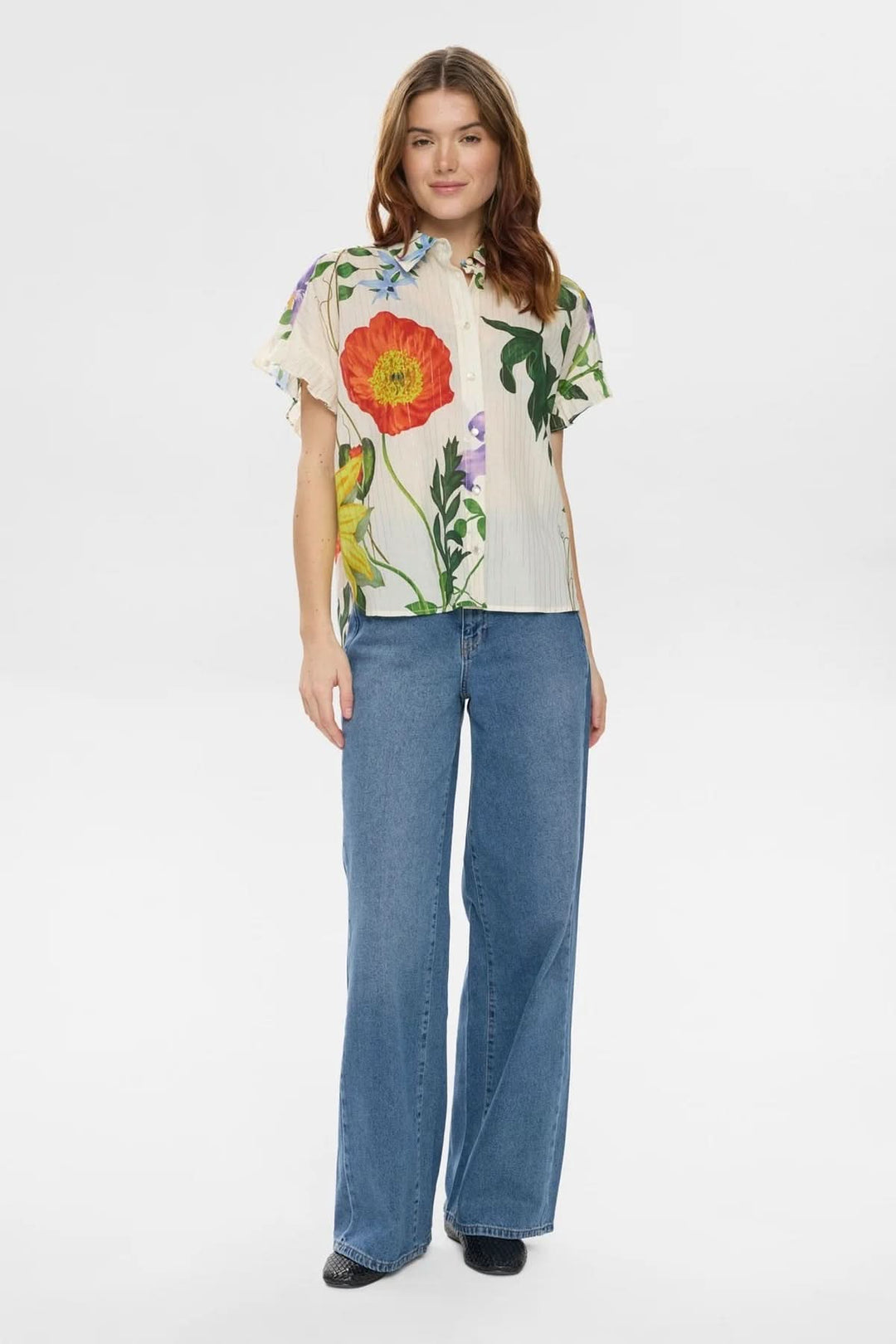 Femme portant une chemise fluide imprimée à manches volantées avec des motifs floraux, col classique, et coupe droite élégante.