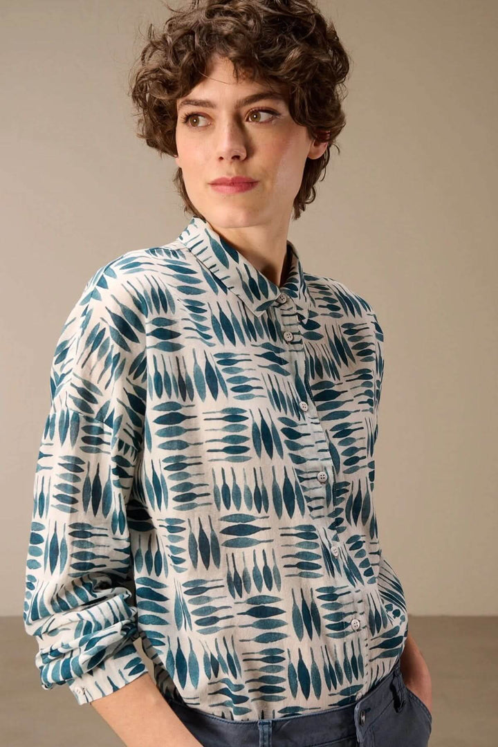 Femme portant une chemise imprimée à manches longues avec motif graphique et col classique, tenue moderne et confortable.