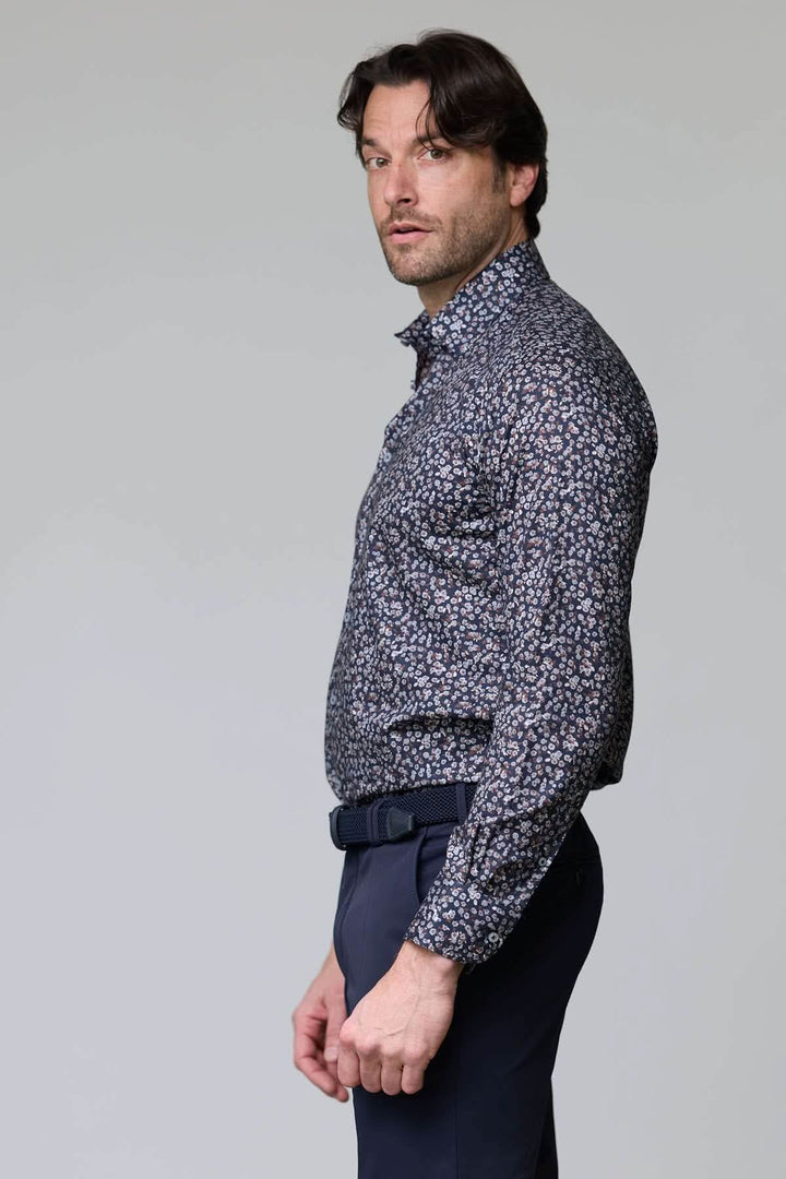 Homme portant une chemise à motif floral abstrait dans des tons contrastés, avec un fond foncé, ajoutant une touche élégante et moderne.