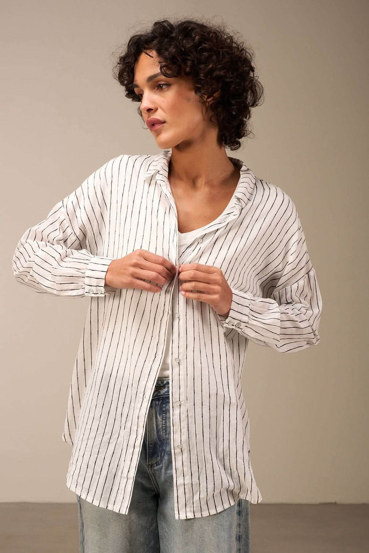 Chemise oversize à rayures verticales avec col classique, portée par une femme aux cheveux bouclés.