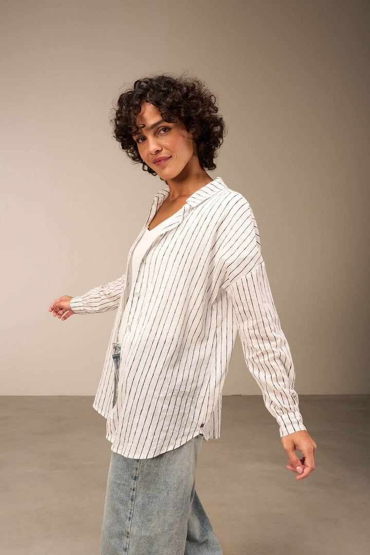 Chemise oversize à rayures verticales portée par une femme, avec col classique et coupe fluide, style casual chic.