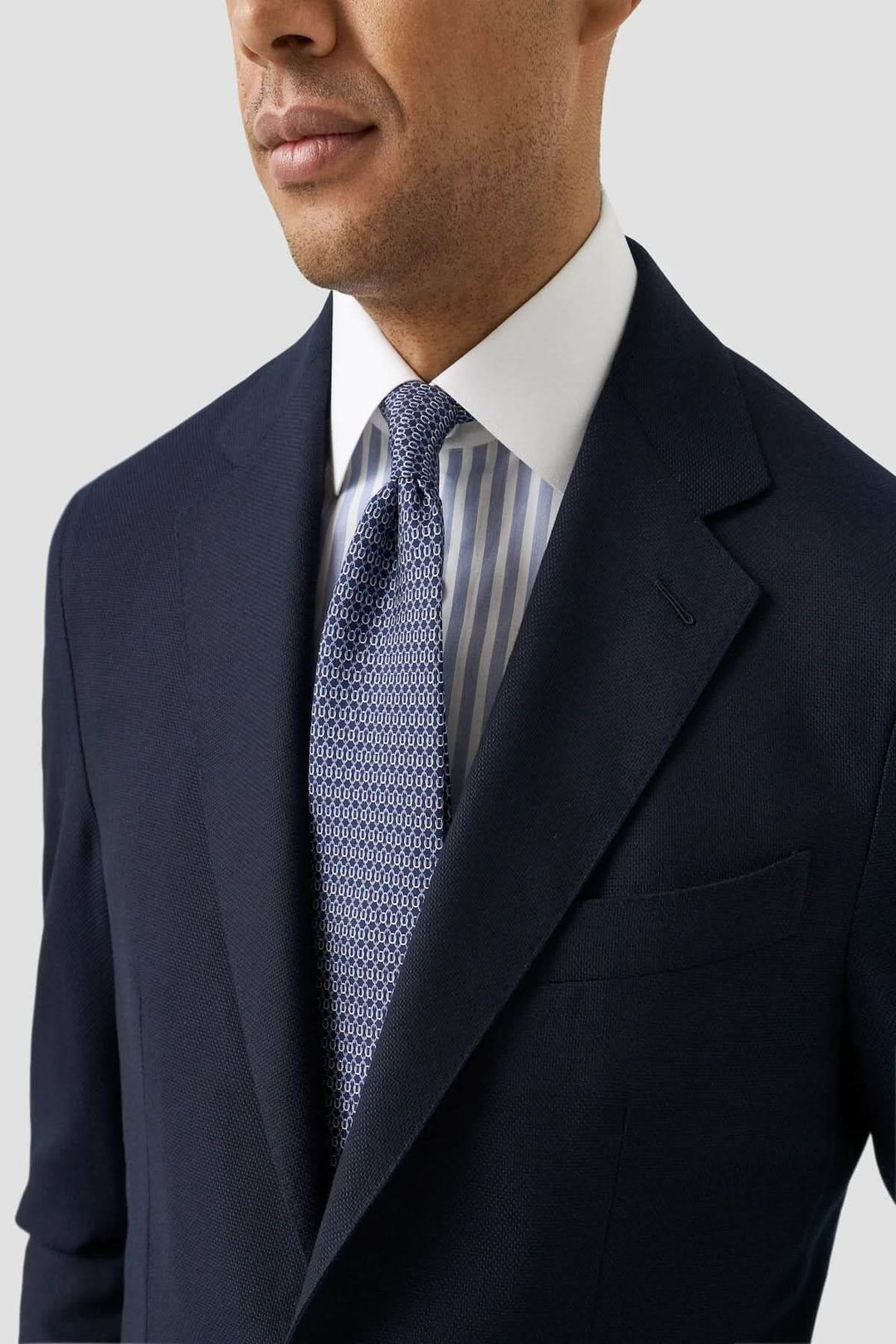 Homme portant une chemise à rayures Bengal à col blanc sous un complet foncé et une cravate texturée.