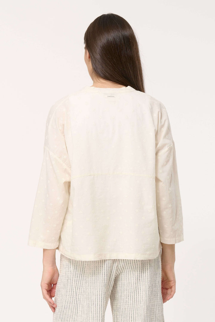 Femme portant une chemise légère en coton brodé, vue de dos, avec un pantalon rayé, élégante et décontractée.