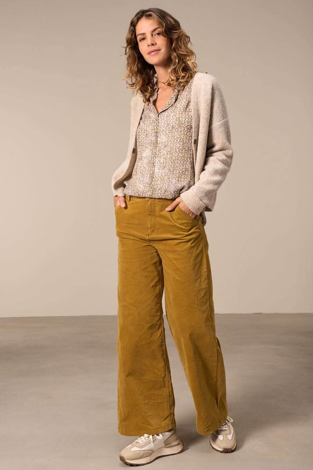 Femme en chemise semi-transparente et pantalon large couleur moutarde, style décontracté et élégant.
