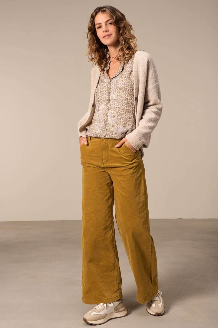 Femme en chemise semi-transparente et pantalon large couleur moutarde, style décontracté et élégant.