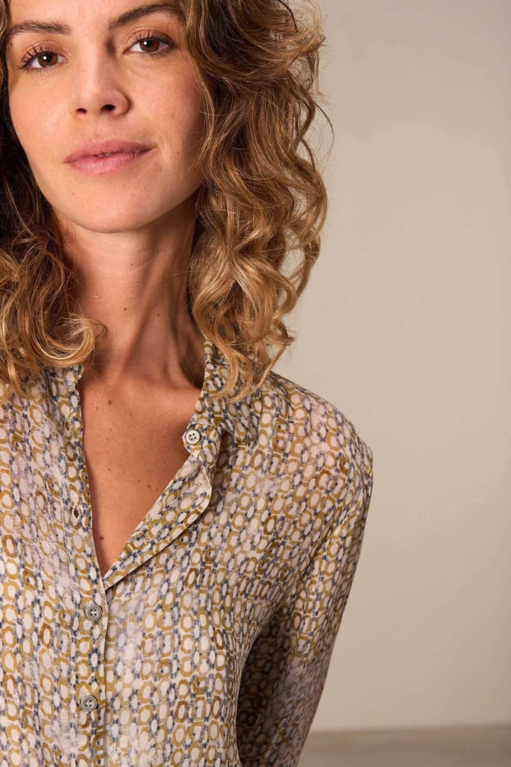 Femme portant une chemise semi-transparente à motifs, manches longues, style élégante et décontracté.