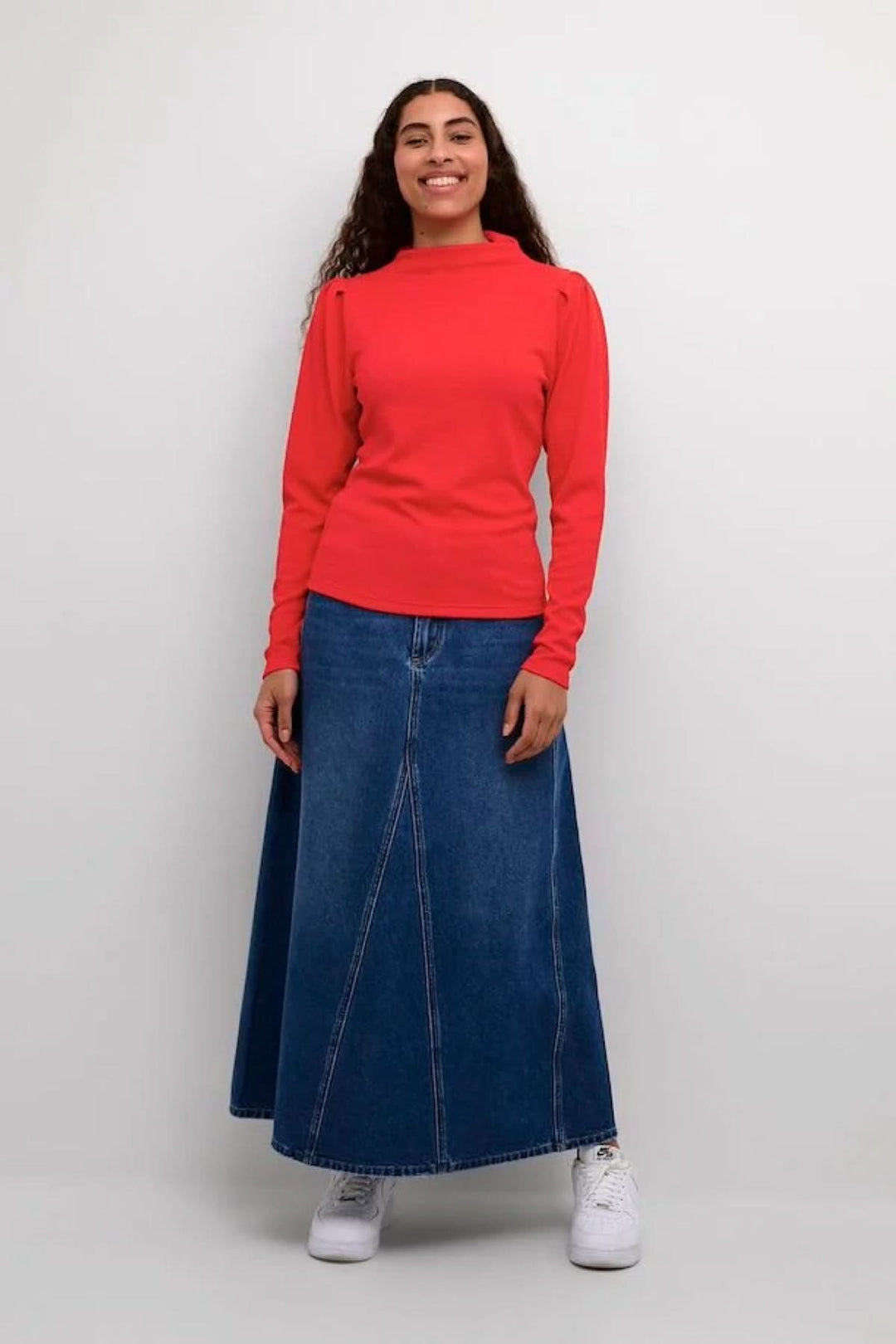 Femme portant un chemisier rouge vif et une jupe en denim, style élégant et décontracté.