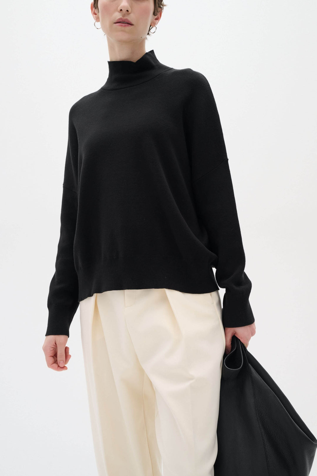Chandail noir à col roulé Tenley, manches longues, porté avec un pantalon beige, stylé et décontracté.