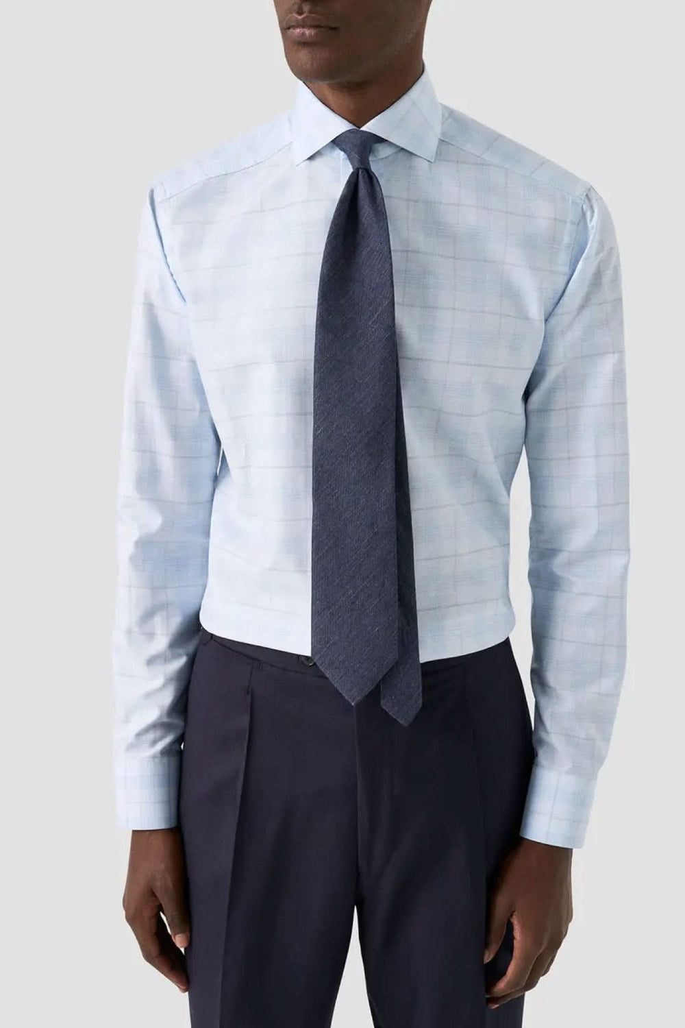 Cravate en lin et soie tissés en une seule pièce portée avec chemise bleue et pantalon sombre, look élégant et moderne.