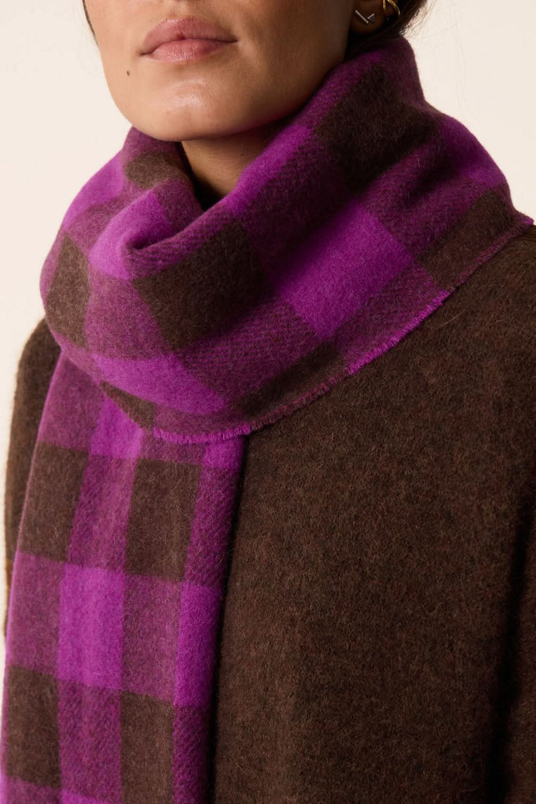 Foulard à carreaux avec des couleurs vives, porté avec un manteau marron pour un look chic et chaleureux.