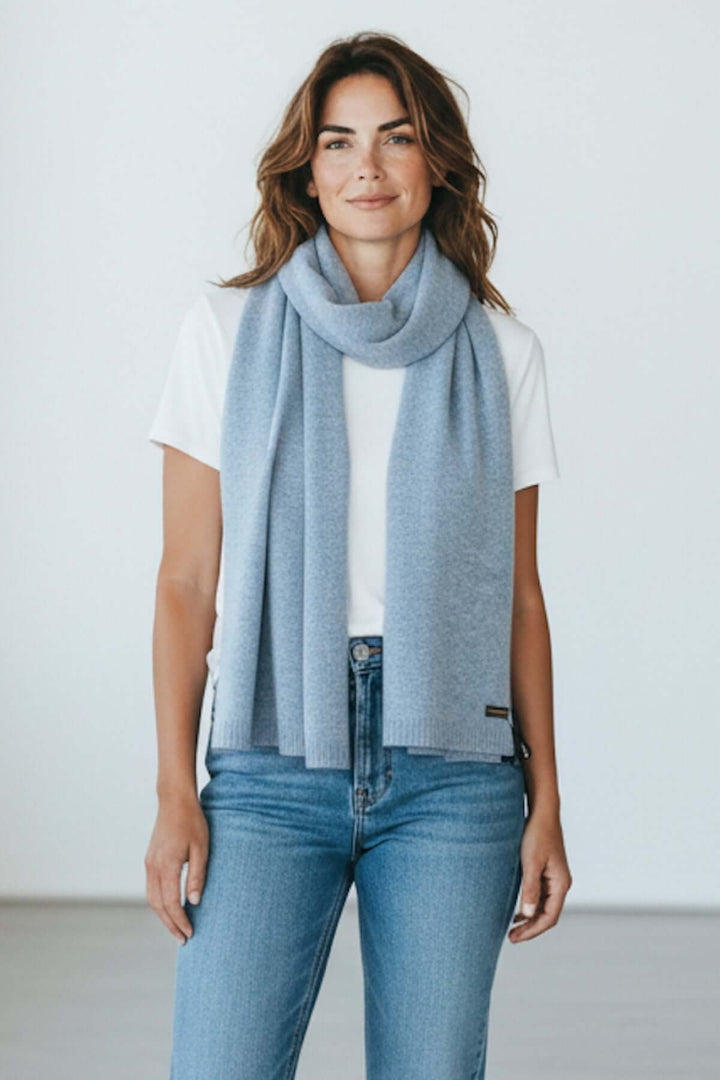 Foulard doux essentiel bleu drapé sur une femme portant un t-shirt blanc et un jean, ajoutant une touche élégante et raffinée.