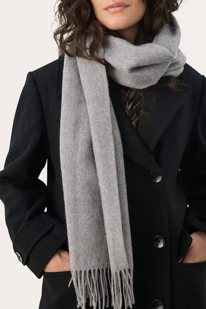 Foulard en laine Kitha gris porté avec un manteau noir, ajoutant chaleur et style aux tenues d'hiver.