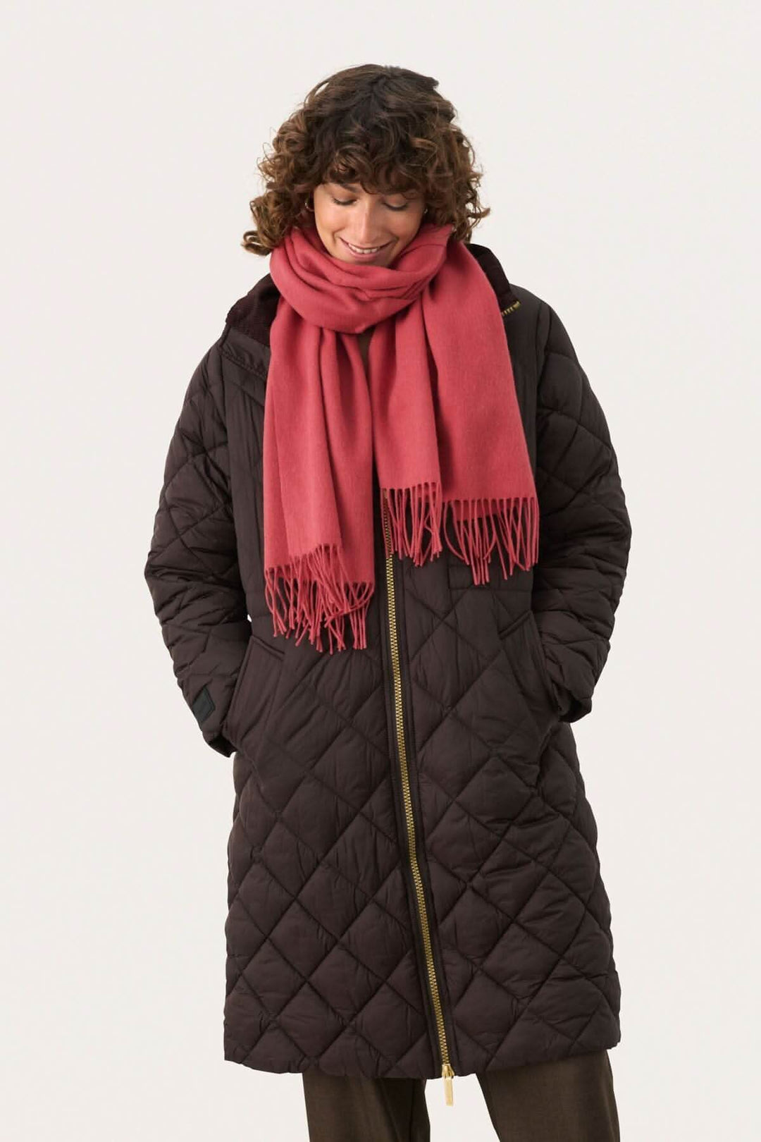 Femme portant une doudoune noire et un foulard en laine rose, souriante et élégante pour l'hiver.