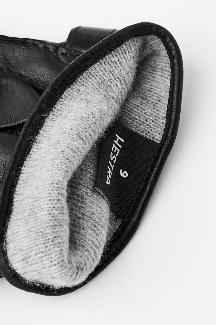 Intérieur d'une paire de gants en cuir noir avec doublure en laine grise, étiquette Hestra visible.