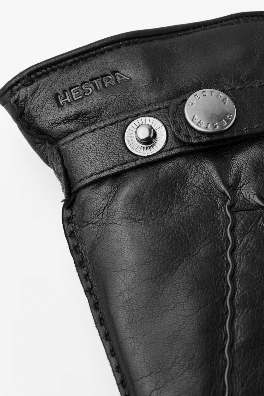 Détail d'une manchette en cuir noir avec boutons pression et logo Hestra.