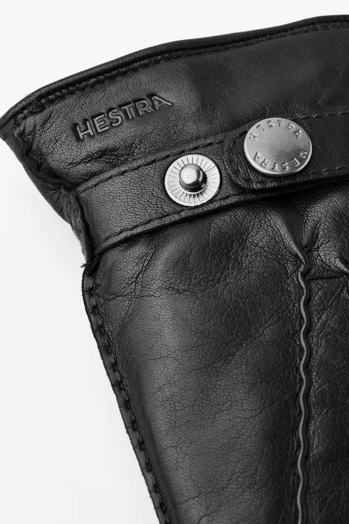 Détail d'une manchette en cuir noir avec boutons pression et logo Hestra.