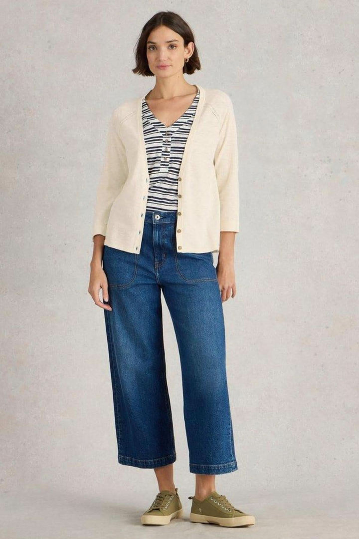 Gilet Col V Naria blanc cassé sur un modèle, associé à un t-shirt rayé et un jean bleu, pour un look décontracté.