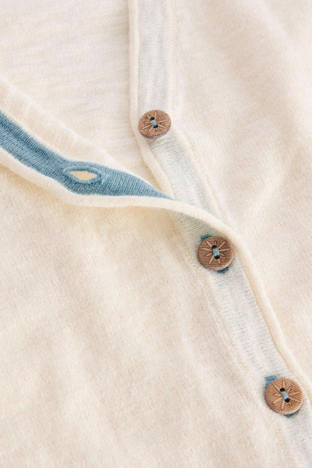 Gilet col V Naria blanc cassé avec boutons marron et bordure bleue, élégant et décontracté.