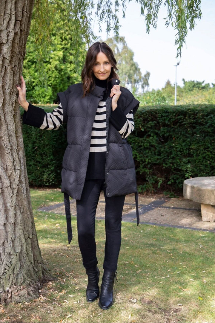 Femme souriante portant un gilet matelassé noir Tahani, debout près d&