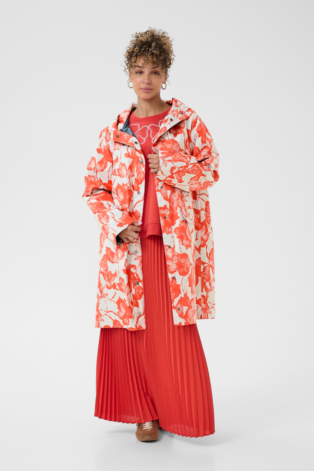 Imperméable Olif avec motif floral expressif, coupe droite, longueur sous le genou, porté sur tenue rouge élégante.
