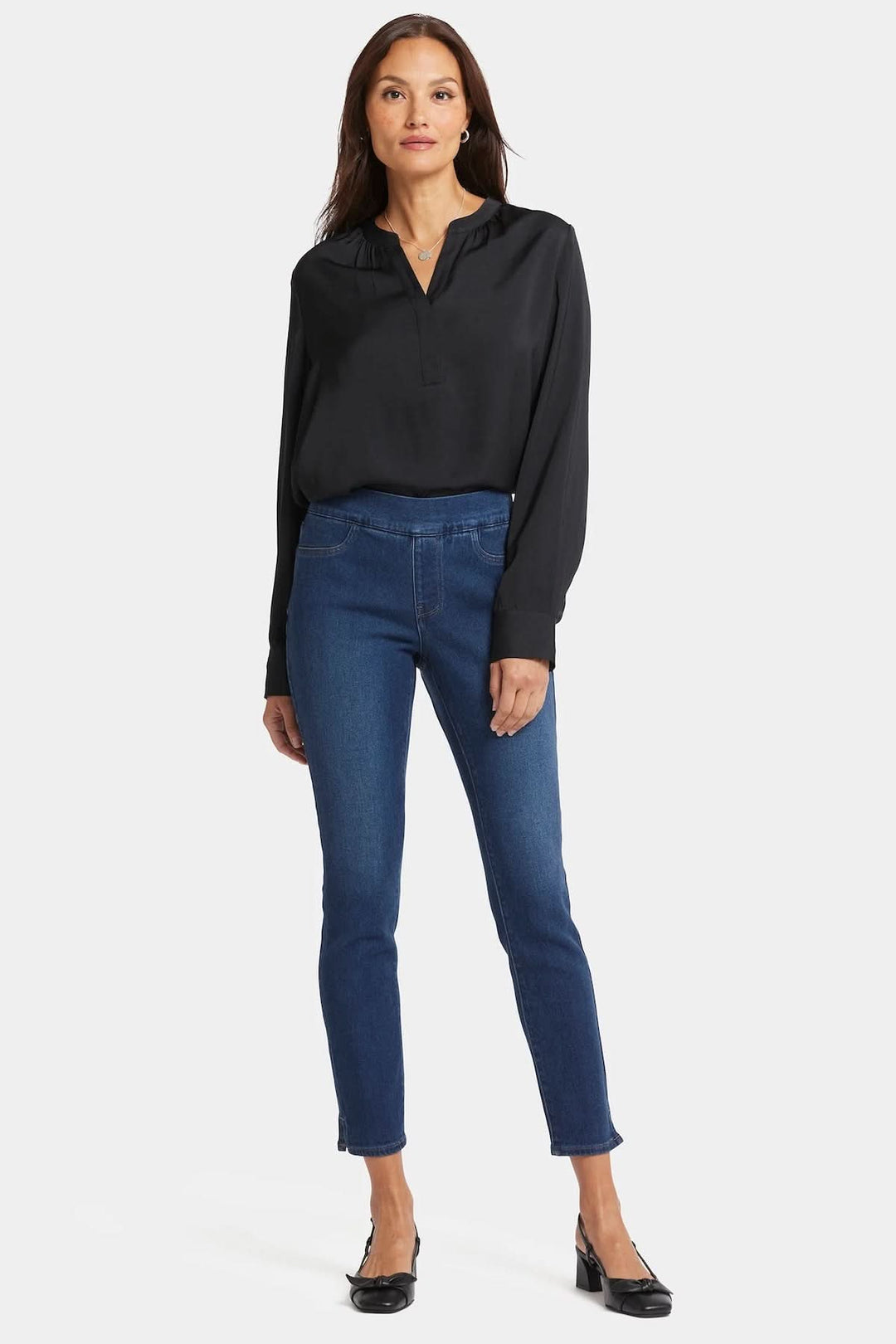 Femme en chemisier noir et jean skinny Alina, mettant en avant une coupe ajustée et une large ceinture à enfiler.