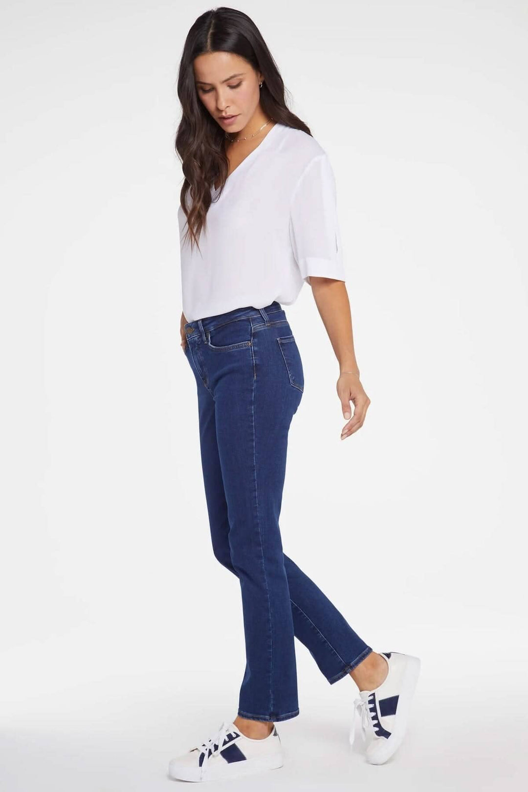 Femme portant le jean Sheri, coupe ajustée, avec un haut blanc et des baskets blanches.