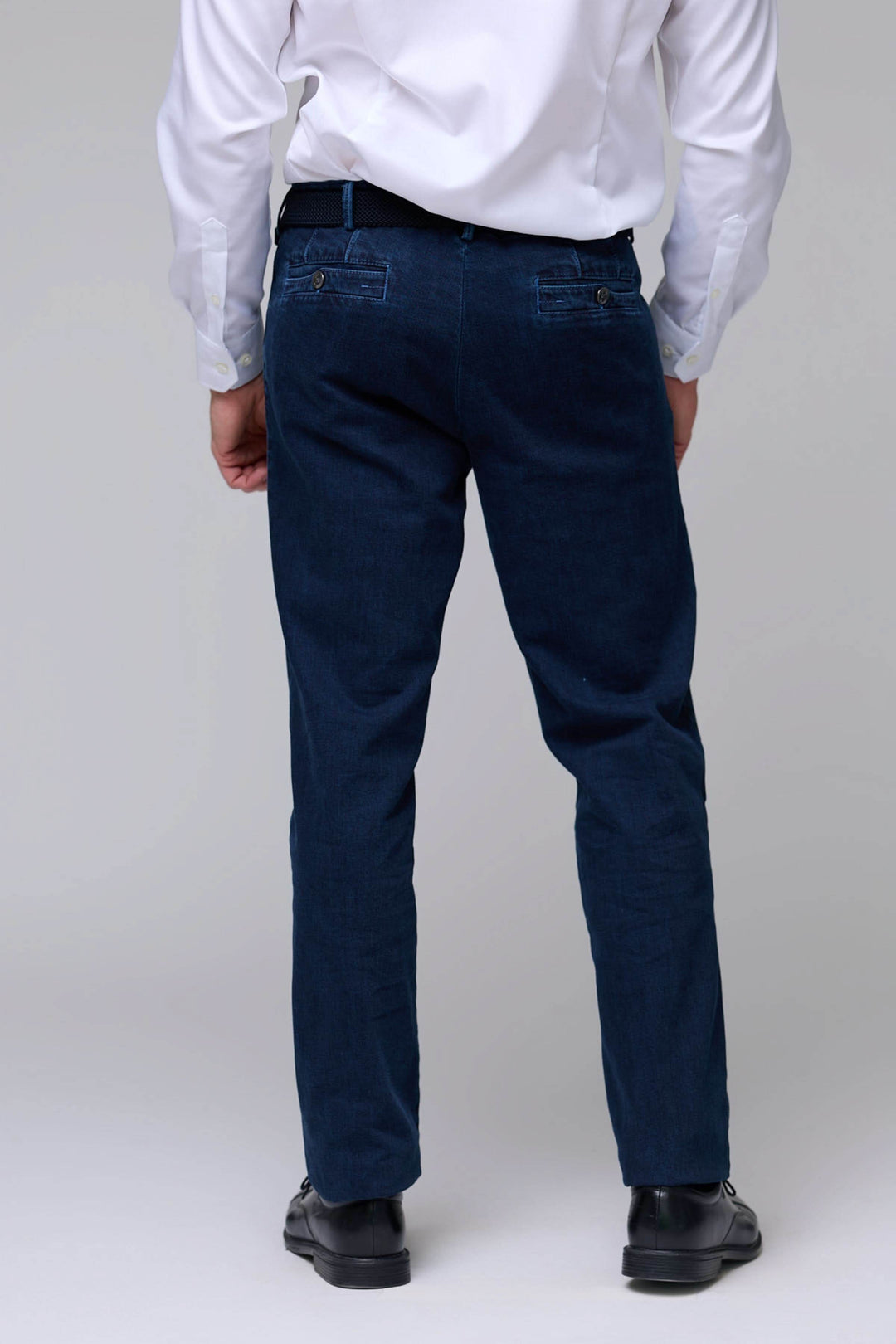 Jean coupe droite en denim extensible avec surpiqûres, vu de dos, porté par un homme en chemise blanche et chaussures noires.