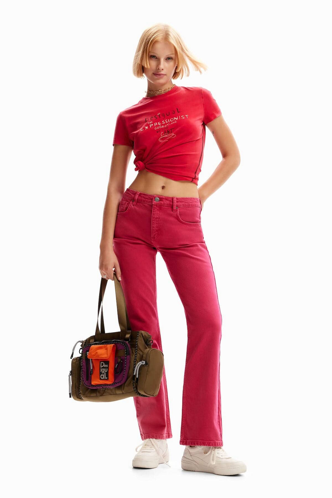 Femme portant un t-shirt rouge et un jean flare rose, avec un sac à main tendance.